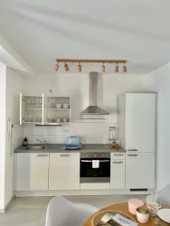 Eine moderne Küche mit weißen Möbeln und einer Edelstahlabzugshaube. Auf der Arbeitsplatte stehen Geschirr und Küchenutensilien bereit.