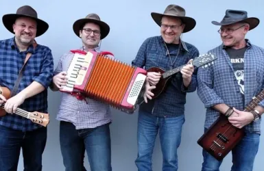 Vier Musiker tragen Hüte und stehen lächelnd zusammen. Einer von ihnen spielt ein Akkordeon, während die anderen verschiedene Instrumente halten.