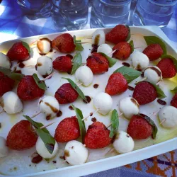 Ein frischer Salat mit Erdbeeren, Mozzarella und Basilikum. Das Gericht ist appetitlich angerichtet und mit Balsamico beträufelt.