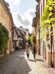 Eine charmante Gasse mit historischen Gebäuden und Pflanzen an den Wänden. Zwei Personen spazieren entspannt die Straße entlang.