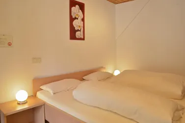 Ein gemütliches Schlafzimmer mit einem Doppelbett und zwei Nachttischen. Sanfte Beleuchtung und eine blühende Wanddekoration schaffen eine entspannte Atmosphäre.