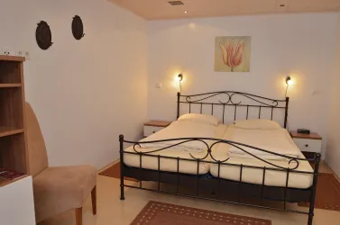 Ein gemütliches Schlafzimmer mit einem Doppelbett und einem Stuhl. Die Wände sind hell gestrichen, und es gibt dekorative Elemente wie ein Gemälde und Wandspiegel.