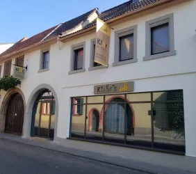 Ein modernes Gebäude mit einer einladenden Fassade. Es zeigt das Schild "Klohr's" und hat große Fenster mit grünen Pflanzen.