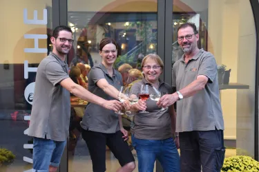 Eine Gruppe von vier Personen toastet mit Gläsern in der Hand. Sie stehen vor einer gläsernen Tür mit einer freundlichen Atmosphäre im Hintergrund.