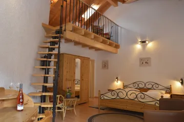 Ein gemütliches Zimmer mit Holzmöbeln und einer offenen Treppe. Die hohen Decken und das natürliche Licht schaffen eine einladende Atmosphäre.