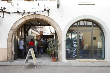 Der Eingang des Weingutes mit zwei offenen Torbögen. Viele Menschen stehen im Hof während eines Festes und genießen die Atmosphäre.