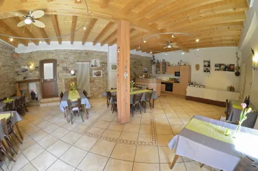 Ein einladendes Restaurant mit Holzdecke und gemütlicher Atmosphäre. Die Tische sind mit bunten Tischdecken und frischen Blumen dekoriert.