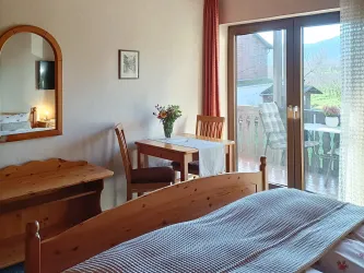 Zimmer 5 mit gemütlicher Sitzecke direkt an der Balkontür – mit Blick ins Grüne.
