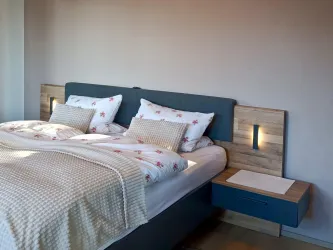 Das Doppelbett in Zimmer 2 mit integrierten Leseleuchten und schwebenden Nachttischen im zeitgemäßen Design.