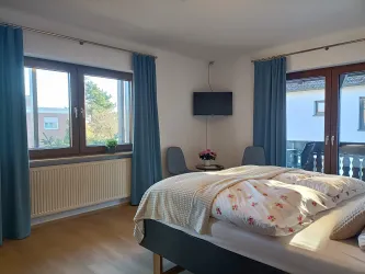 Zimmer 2 ist hell und freundlich, mit großen Fenstern, Fernseher, Sitzecke und Zugang zum Balkon.