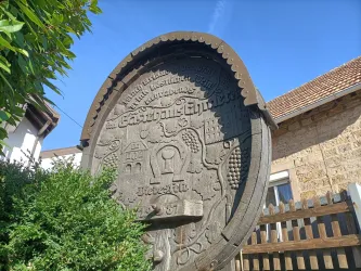 Ein kunstvoll geschnitzter Fassboden mit Weinreben und Inschrift schmückt das Gästehaus an der Weinstraßenmitte – ein Zeichen der Verbundenheit mit der Pfälzer Weinkultur.