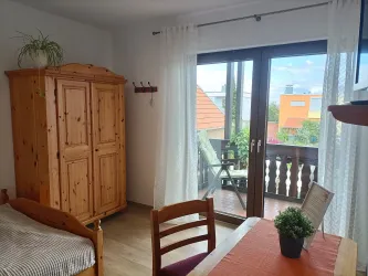 Zimmer 1 bietet einen großen Holzkleiderschrank, einen kleinen Tisch und eine Tür mit direktem Zugang zum Balkon.