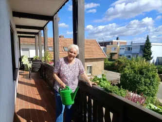 Gründerin Marianne Ehmer pflegt die Blumen auf dem Balkon des Gästehauses an der Weinstraßenmitte. Vom Holzbalkon blickt man über die Dächer von Diedesfeld.