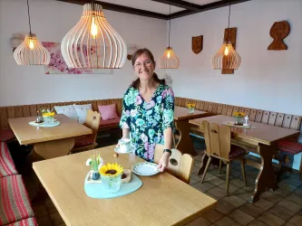 Inhaberin Nicole Ehmer im Frühstücksraum des Gästehauses an der Weinstraßenmitte in Diedesfeld. Holztische, Eckbänke und warmes Licht schaffen eine gemütliche Atmosphäre für den Start in den Tag.