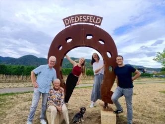 Die Gastgeberfamilie des Gästehauses an der Weinstraßenmitte in Neustadt-Diedesfeld, von links: Inhaber Matthias Ehmer, Gründerin Marianne Ehmer, Tochter Theresa Hoefer, Inhaberin Nicole Ehmer und Schwiegersohn Daniel Hoefer mit Familienhund Dori vor dem Hufeisen-Denkmal am Weinberg.