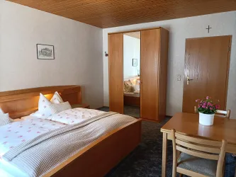 Zimmer 3 mit Doppelbett, Kleiderschrank und kleinem Tisch – Platz für ein Glas Pfälzer Wein am Abend.