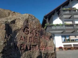 Ein Sandsteinfindling mit rot ausgelegter Inschrift begrüßt Gäste vor dem Gästehaus an der Weinstraßenmitte in Neustadt-Diedesfeld, am Mittelpunkt der Deutschen Weinstraße.