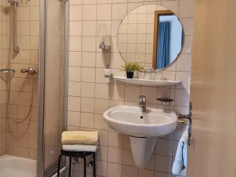 Zimmer 2 hat ein eigenes Duschbad mit WC, Waschbecken und rundem Spiegel.
