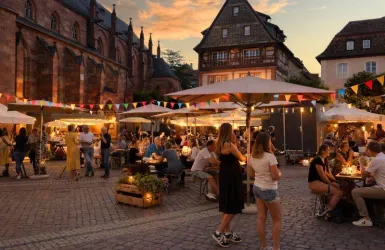 Ein lebhaftes Marktgeschehen bei Sonnenuntergang mit Menschen, die an Tischen sitzen. Bunte Dekorationen und Lichter schaffen eine angenehme Atmosphäre.
