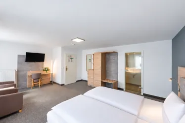 Ein modernes Hotelzimmer mit zwei Einzelbetten und einem Fernseher. Es gibt eine gemütliche Sitzecke und ein angrenzendes Bad.