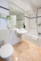 Ein modernes Badezimmer mit einer Badewanne und einem Waschbecken. Die Wände sind gefliest und es gibt dekorative Pflanzen.