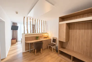 Ein modernes Zimmer mit Holzdekor und einem kleinen Arbeitsplatz. Große Fenster lassen viel Tageslicht herein.