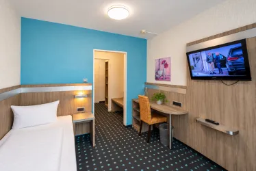 Ein modernes Hotelzimmer mit einem Einzelbett und einem Schreibtisch. Die Wände sind in ruhigen Farben gehalten, und ein Fernseher ist an der Wand montiert.