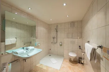 Ein modernes Badezimmer mit hellen Fliesen und einer Dusche. Der Waschbereich ist gut ausgestattet mit Handtüchern und einem großen Spiegel.