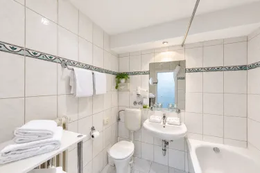 Ein modernes Badezimmer mit weißen Fliesen und einem großen Spiegel. Es enthält eine Badewanne, ein Waschbecken und frische Handtücher.