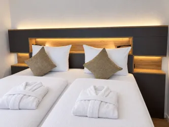 Ein modernes Schlafzimmer mit zwei Betten und Kissen. Die warme Beleuchtung und die weißen Handtücher verleihen einen einladenden Eindruck.
