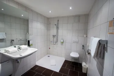 Ein modernes Badezimmer mit weißen Fliesen und dunklem Boden. Es enthält eine Dusche, ein Waschbecken und eine Toilette.