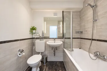 Ein modernes Badezimmer mit einer Badewanne, einer Dusche und einem Waschbecken. Die Wände sind hell gefliest und es gibt einige grüne Pflanzen zur Dekoration.