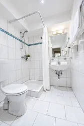 Ein modernes Badezimmer mit weißen Fliesen und einem Duschbereich. Die Ausstattung umfasst eine Toilette, ein Waschbecken und einen Spiegel.