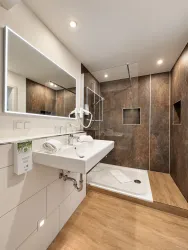 Ein modernes Badezimmer mit einer begehbaren Dusche und einem eleganten Waschbecken. Die Wände sind in dunklen Farben gehalten, und es gibt viel Tageslicht durch den großen Spiegel.