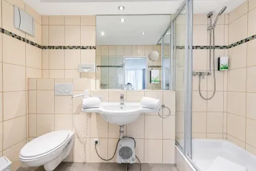 Ein modernes Badezimmer mit hellen Fliesen und einer Dusche. Es gibt ein Waschbecken, eine Toilette und einen großen Spiegel.