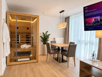 Ein modernes Zimmer mit einer Sauna und einem Esstisch. Der Raum ist hell und freundlich mit großen Fenstern.