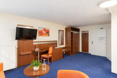 Ein modern eingerichtetes Zimmer mit einem Fernseher, einem Tisch und zwei Stühlen. Die Wände sind in neutralen Tönen gehalten, und ein Kunstwerk verziert die Wand.