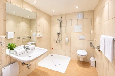 Ein modernes Badezimmer mit hellen Fliesen und einer Dusche. Es gibt ein Waschbecken, Toilettenpapier und frische Handtücher.