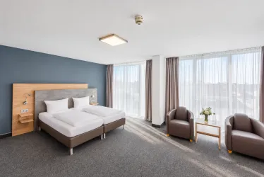 Ein modernes Zimmer mit zwei Einzelbetten und großen Fenstern. Es gibt gemütliche Sessel und einen Tisch neben dem Bett.