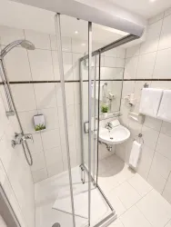 Ein modernes Badezimmer mit einer gläsernen Dusche und einer weißen Handwaschbecken. Frische Handtücher und eine kleine Pflanze vervollständigen das gepflegte Ambiente.