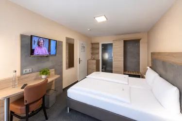 Ein modernes Hotelzimmer mit einem Doppelbett, einem Schreibtisch und einem Fernseher. Das Zimmer ist hell und gemütlich eingerichtet.