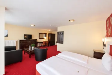 Ein modernes Hotelzimmer mit zwei Betten und einem gemütlichen Sitzbereich. Der Boden ist rot, und es gibt einen Fernseher sowie einen Tisch im Raum.