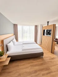 Ein modernes Hotelzimmer mit zwei Betten und einem eleganten Holzelement. Vor den Fenstern strömt viel natürliches Licht hinein.