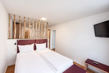 Ein modernes Schlafzimmer mit zwei Einzelbetten und einem Fernseher. Die Wand ist mit Holzstämmen dekoriert, was eine natürliche Atmosphäre schafft.