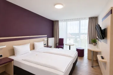 Ein modernes Hotelzimmer mit zwei Einzelbetten und einer großen Fensterfront. Der Raum ist in sanften Farben gestaltet und bietet einen angenehmen Blick nach draußen.