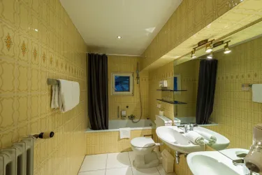 Ein Badezimmer mit gelben Fliesen und einer modernen Ausstattung. Die Umgebung ist hell erleuchtet und bietet eine Dusche sowie ein Waschbecken.