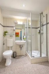 Ein modernes Badezimmer mit Dusche, Waschbecken und WC. Helle Fliesen und eine ordentliche Ausstattung sorgen für eine angenehme Atmosphäre.