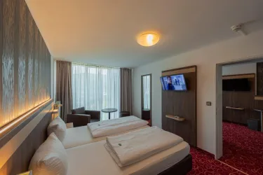 Ein modernes Hotelzimmer mit zwei Einzelbetten und einem großen Fenster. Die freundliche Atmosphäre wird durch den roten Teppich und die stilvolle Einrichtung unterstrichen.