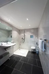 Ein modernes Badezimmer mit Dusche, Waschbecken und Toilette. Die Wände sind hell gefliest und der Boden ist aus dunklen Fliesen.