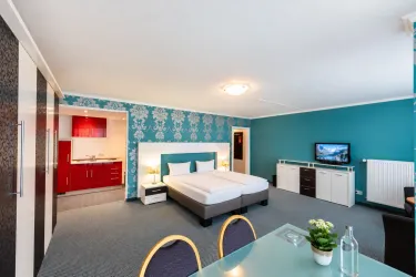 Ein modernes Zimmer mit zwei Einzelbetten und bunten Wänden. Es gibt eine kleine Küchenecke und einen Essbereich.